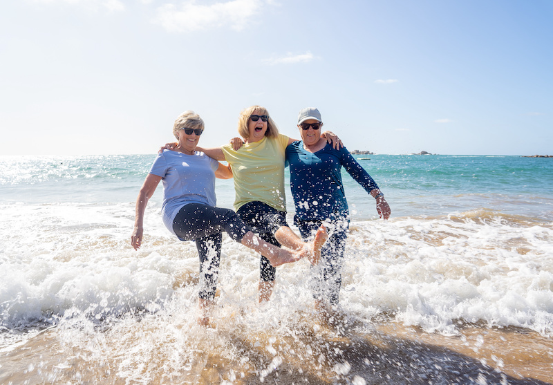 Three older women joyfully kicking in the surf