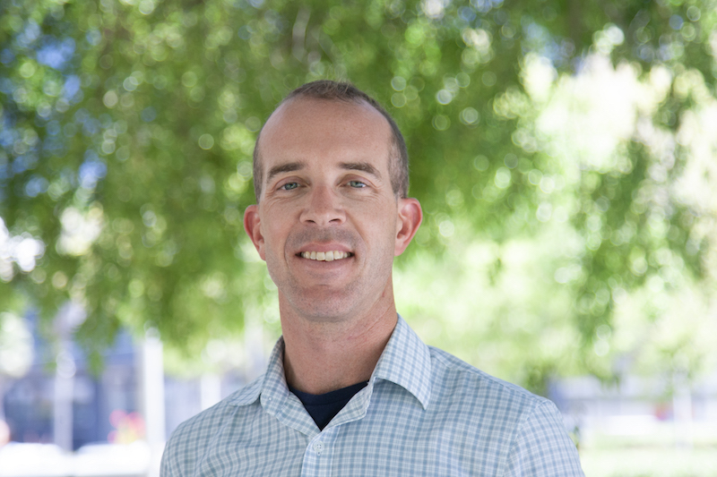 Close-up of Aaron Colverson under a tree smiling at camera