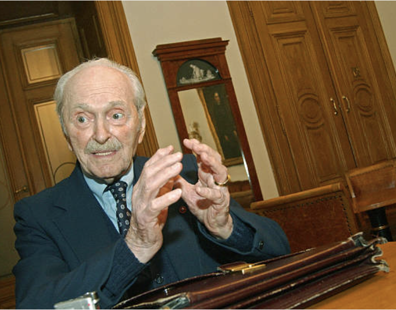 An older man in a suit speaking animatedly to someone off camera