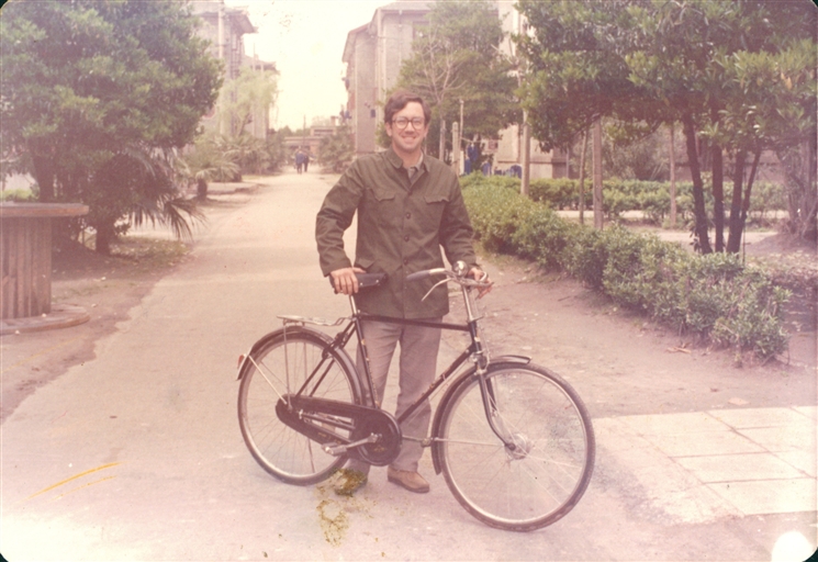 Tom Gold in 1979 posing holding his bicycle on a bike path at Fudan University