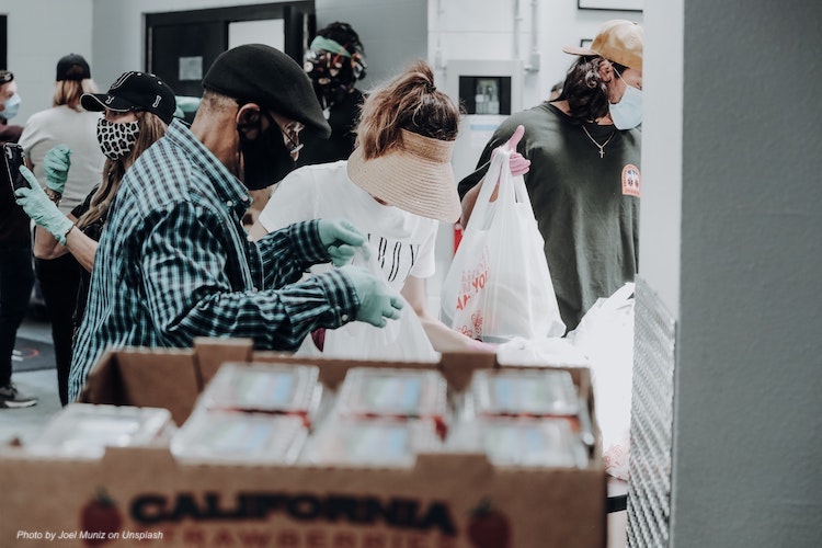 Masked people filling bags with food in a work area